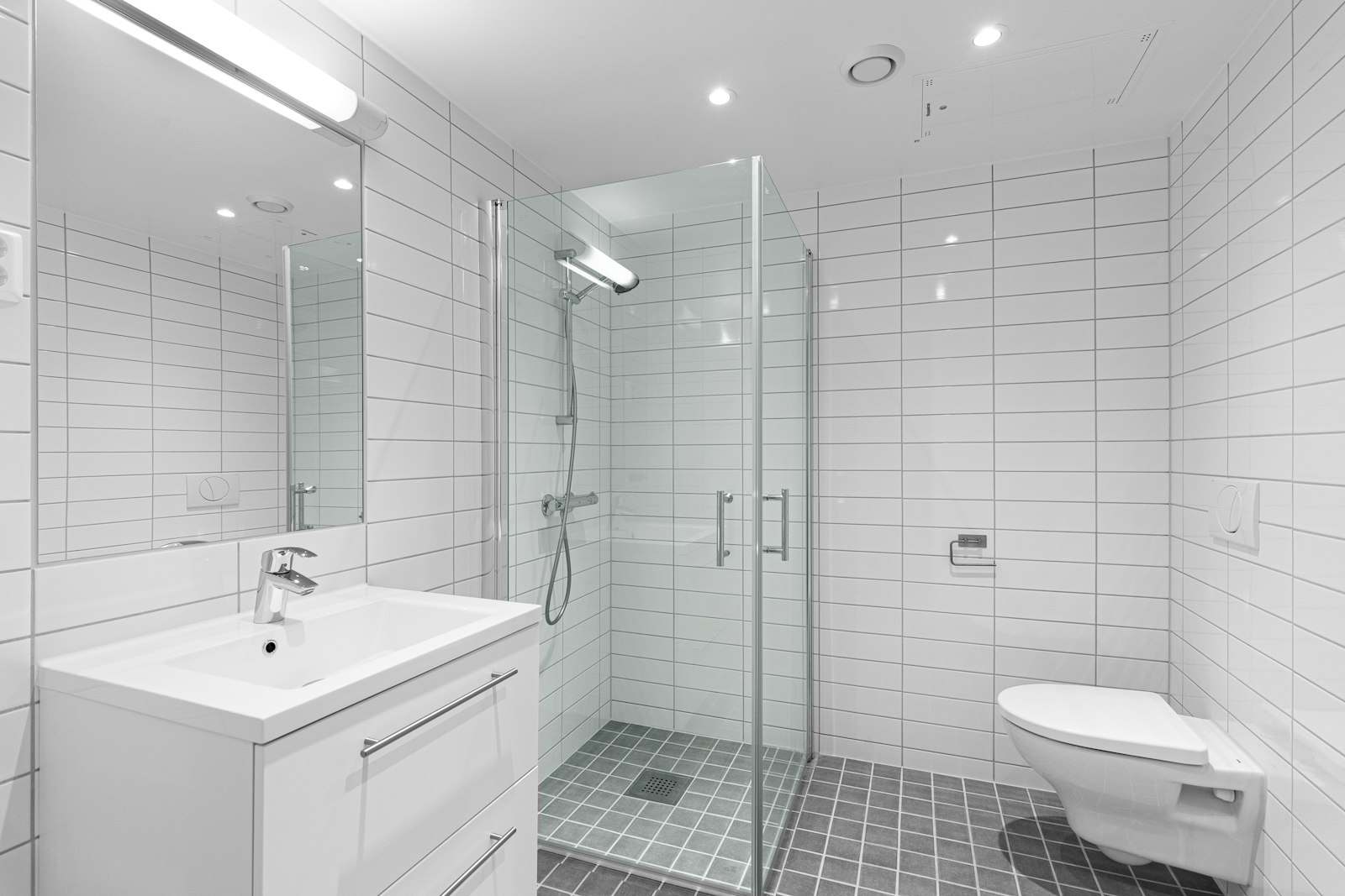 Baño blanco con ducha a ras de suelo y mampara de cristal